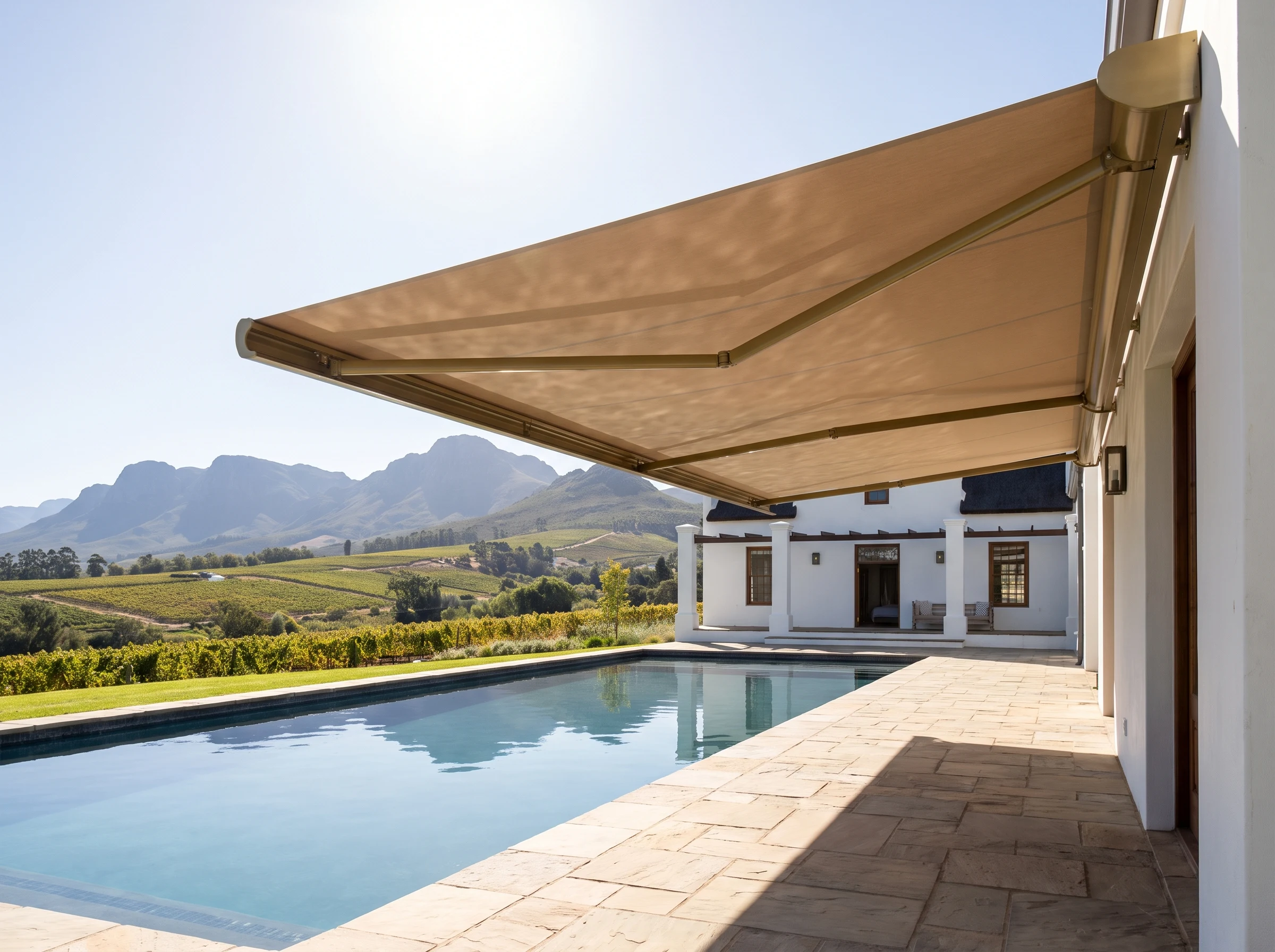 A wide folding-arm awning extended over a pool deck at a Cape Winelands estate home, mountains beyond