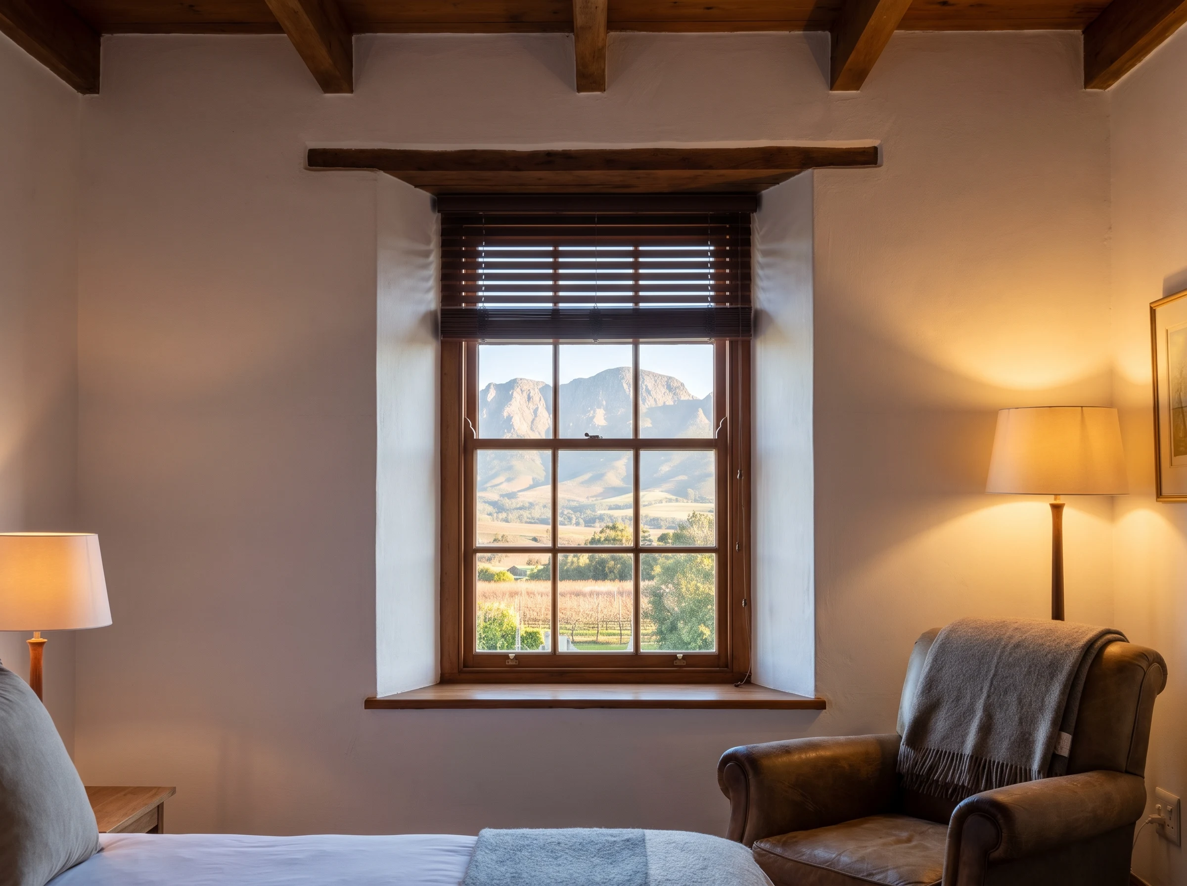 Deep-set sash window fitted with a timber venetian blind in a restored Cape Dutch-style Franschhoek estate homestead, mountains through the glass