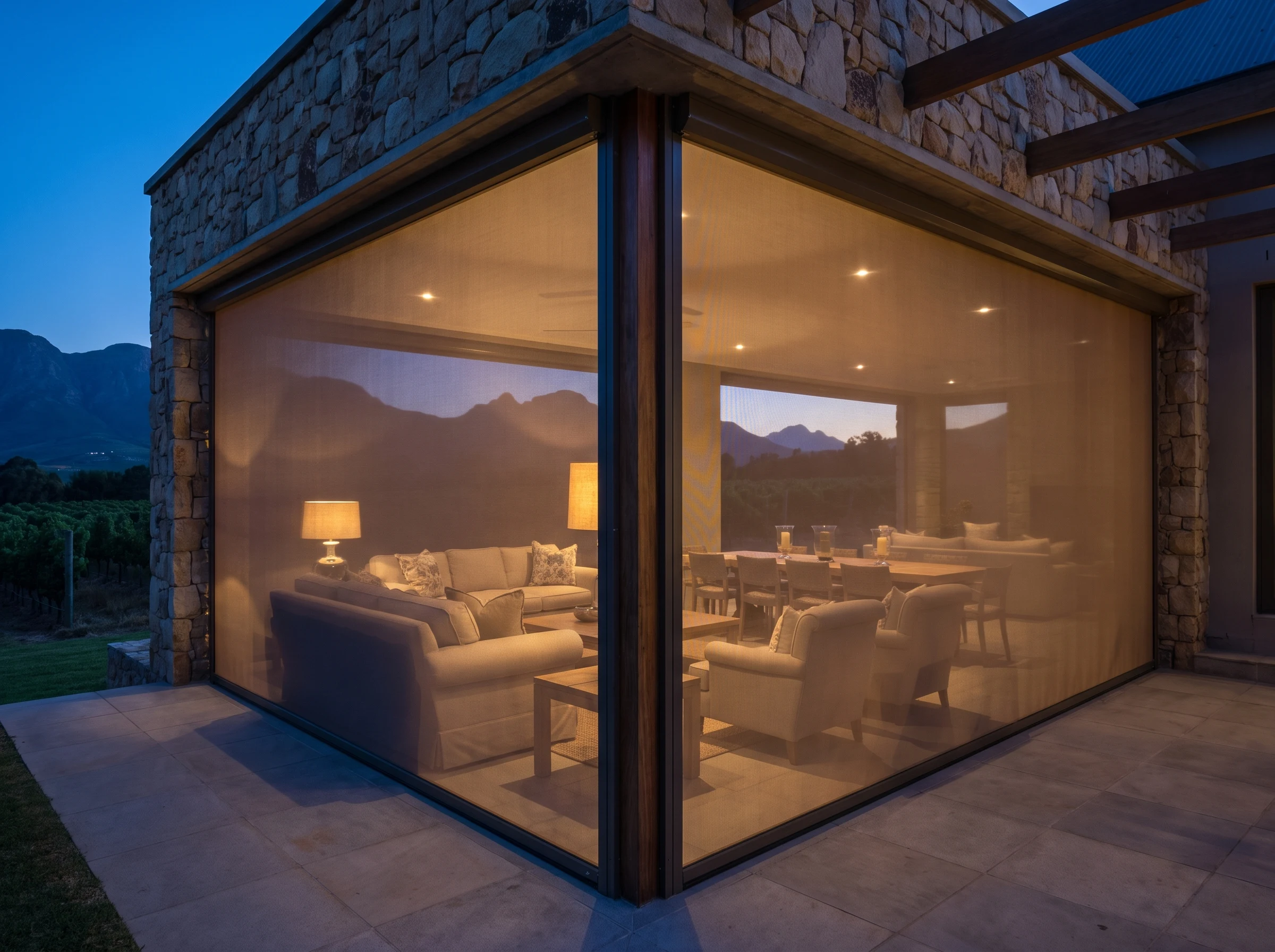 A fully enclosed outdoor entertaining room on a Cape Winelands estate terrace with zip-track screens closed against the evening